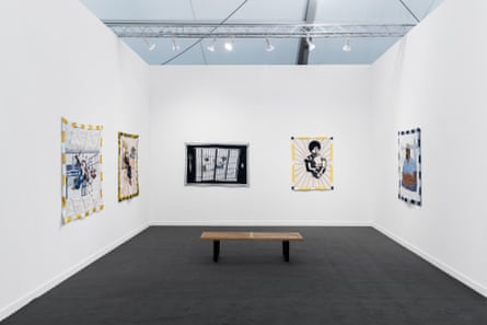 four quilts on a white wall in an empty room with a bench. images include a person behind bars and a person grimacing while surrounded by black lines like a sun