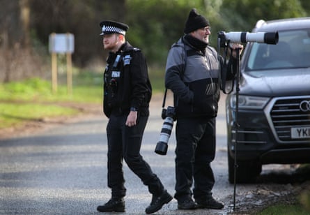 A police officer walks next to a press photographer near the royal estate at Sandringham, Norfolk