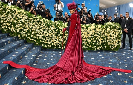 Taylor wears a red flowy outfit with matching hat at the Met Gala in 2025.