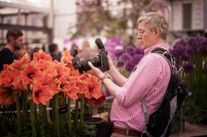 A man with a hefty camera photographs a big red flower