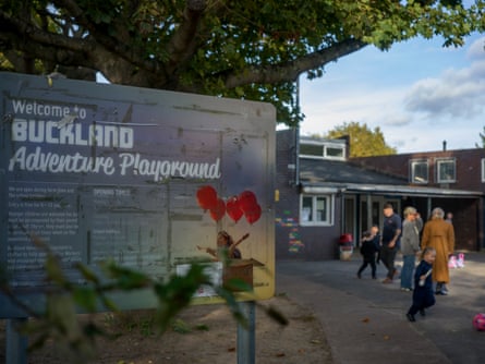 A sign saying ‘welcome to Buckland adventure playground’ with adults and children by a building in the background