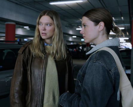Léa Seydoux and Jella Haase stand close together in a dimly lit parking garage