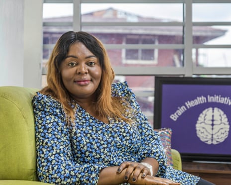 Portrait of a black woman sitting in a chair next to a computer with a screensaver reading: 'Brain Health Initiative Nigeria'