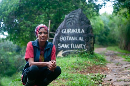 A woman crouches in front of a stone bearing the words Gurukula Botanical Sanctuary