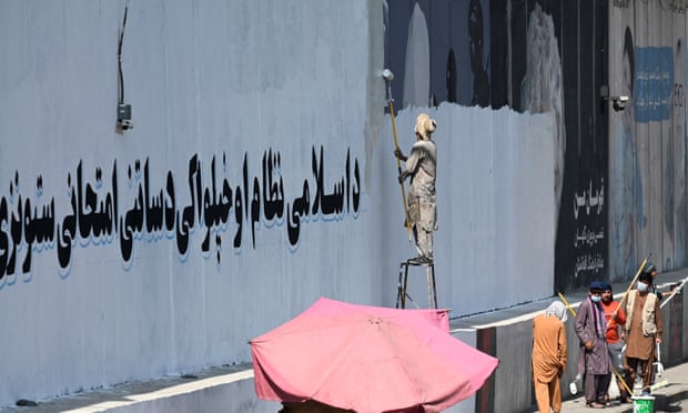 A man paints over murals on a concrete wall in Kabul with a message reading ‘For an Islamic system and independence, you have to go through tests and stay patient’.
