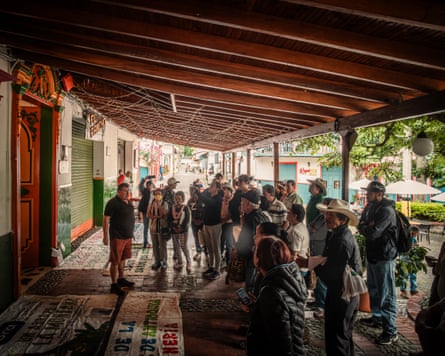 A crowd of people, some in straw cowboy hats, seen standing around a large colourful banner laid out on a veranda as someone talks to them