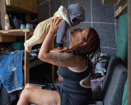 A woman sitting in a chair lifts her baby in the air above her face.
