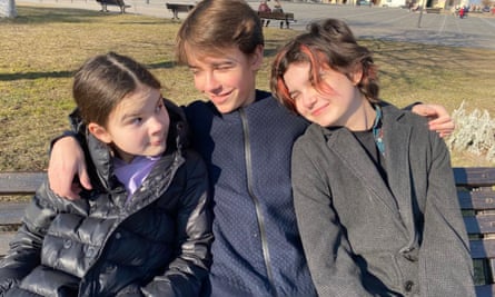Padalko’s children Katia, 11, Mykhailo, 15, and Maria, 13, sitting on a bench hugging.