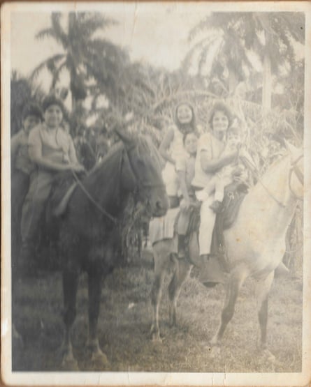 Old black and white photograph of two horses with women and children sitting on them, in front of tropical-looking trees
