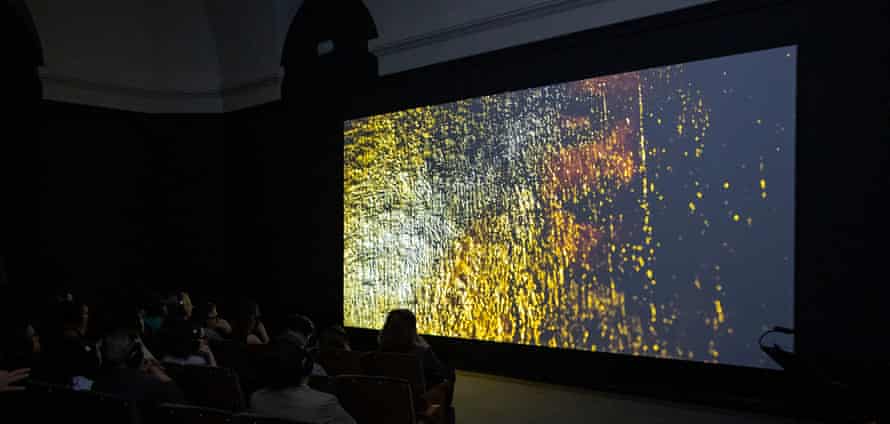 A screen shows a gold-flecked wall in a small cinema