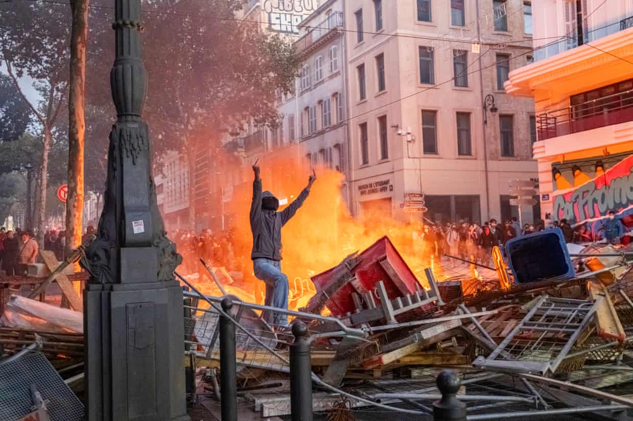 A protester gives the police the middle finger in front of burning barricades in Marseille.