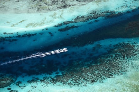 Aerial view of a boat leaving a wake trail behind it as it crosses the ocean. Reefs and sand are visible under the water
