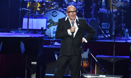 Harry Hill, microphone in hand, performing on stage. 