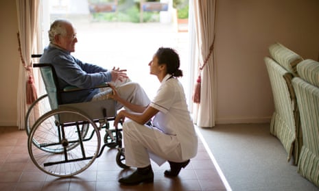 A care home staff member kneeling beside an older man in a wheelchair