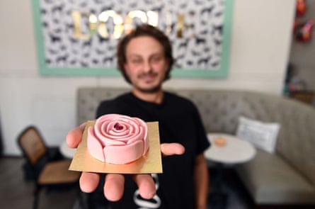 A man displays a pink, rose-shaped food item in an outstretched hand.