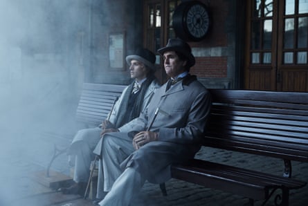 Two men on a bench on a railway platform as smoke billows in
