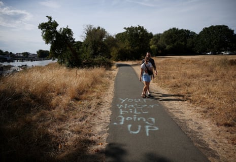 A couple walks past a spray-painted message from the "Save Our Lands and River" community campaign opposing Thames Water's Teddington Direct River Abstraction (TDRA) scheme, which would take 75m litres of drinking water a day from the River Thames at Teddington during droughts and replace it with treated wastewater pumped from Mogden Sewage Treatment Works into the river, in London.