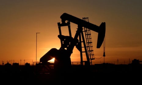 A pump jack operates in front of a drilling rig at sunset in an oil field in Midland, Texas US
