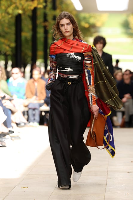 A model in large baggy trousers with colourful tight top with scarf motifs, and a large colourful scarf
