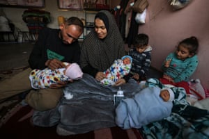 Ammar and Iman al-Masri hold three babies while sitting on the floor, as two older children sit behind