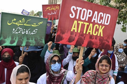 People march down a street holding placards. One in English reads ‘stop acid attack’.