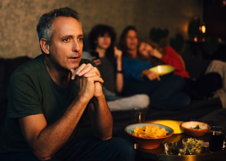 Hopeful man praying while watching sports in living room at night, with a big tray of snacks next to him.