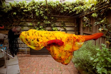 A person in a yellow floral outfit appears to float horizontally above a brick courtyard