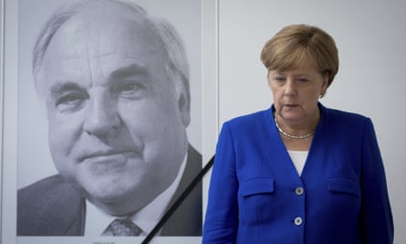 Angela Merkel looking sombre next to a big photo on the wall of Helmut Kohl