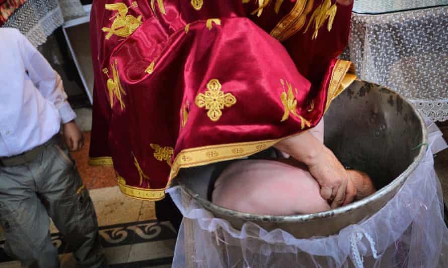 A Romanian Orthodox priest sinking a child in holy water during baptism, in a church in Bucharest