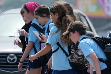 A school girl uses her phone as she walks with a group of children