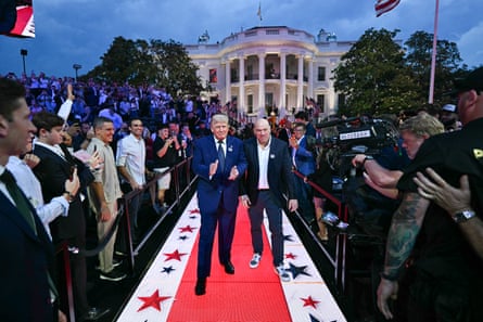 two men walk side by side on a red carpet between rows of people