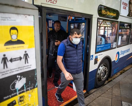 Passengers alight from a bus at Piccadilly Gardens, Manchester; a man stepping out is wearing a face mask. There is a sign indicating social distancing to the side at the bus stop.
