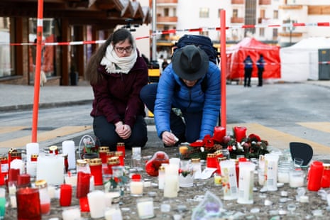 A man lights a candle next to the tributes laid for the victims outside Le Constellation bar in Crans-Montana.