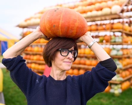 Emma Beddington holds a pumpkin on her head in front a huge display of pumpkins on wooden shelving in the shape of a house