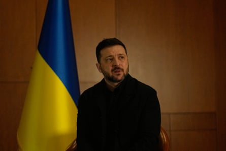 Volodymyr Zelenskyy sitting next to a Ukrainian flag