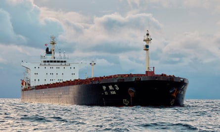 large cargo ship with black hull and its name in Chinese and European lettering; it is anchored in a grey, wintry-looking sea against a cloudy sky