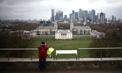 A person takes a photograph from Greenwich Park, with the Canary Wharf financial district in the distance, in London.
