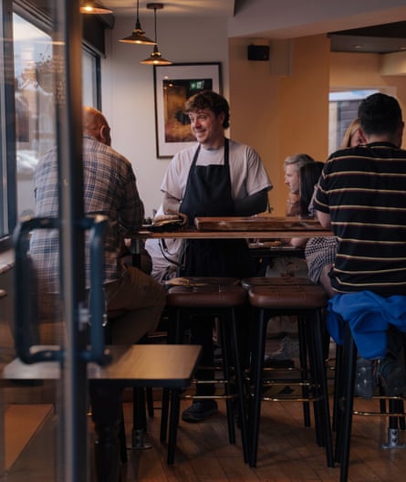 Men sit at tables in a pub in Wales while the owner chats to them