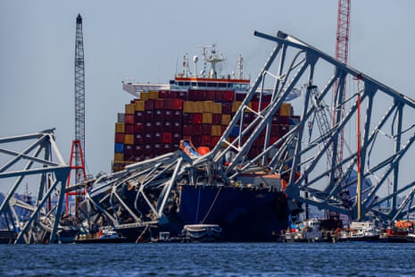A large container ship with the remains of a metal bridge strewn around and on it.
