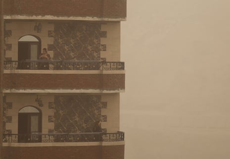 Woman on balcony of flats in sandstorm.