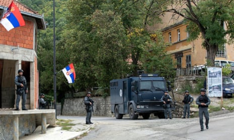 Armed police in bulletproof vests stand around a police truck under Kosovan flags