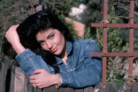 Singer/actress Apollonia is shown in a head and shoulders outdoors portrait, leaning on a fence.