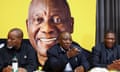 Cyril Ramaphosa points his finger forward next to Paul Mashatile in his right and Gwede Mantashe on his left. All are sat in front of a large yellow picture of Ramaphosa on a bright yellow background.