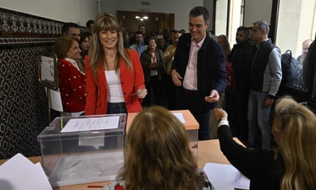 Pedro Sánchez and Begoña Gómez about to place their ballots in containers as election officials look on and with a crowd of people assembled behind