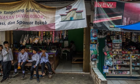 Indonesian schoolchildren at a food stall with an anti tobacco banner, next to stalls with cigarette advertising and products on sale opposite thei school.
