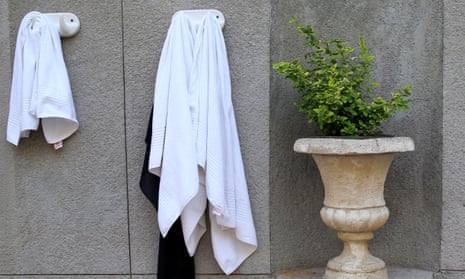 Two towels hanging on ceramic hooks on a marble wall next to a marble urn with a plant in it