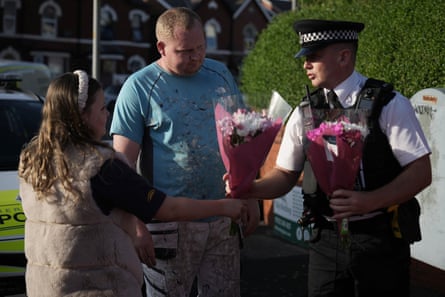 A police officer receives two bouquets of flowers from a man and a woman