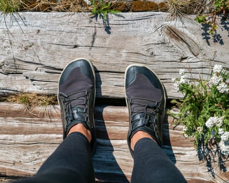 Person stood on a wooden platform wearing barefoot hiking shoes on a sunny day.