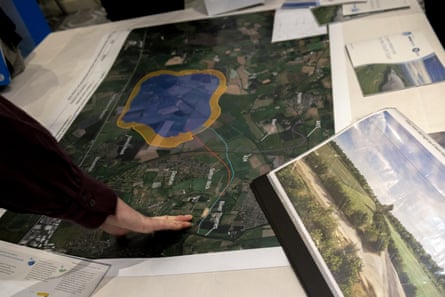 An anonymous hand reaches out to a map and other plans for a reservoir laid out on a table