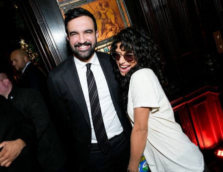 Zohran Mamdani in dark suit and tie standing close to Odessa A’zion